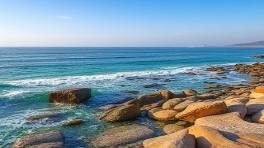 tranquil HuaHin landscape, serene, panoramic coastal view, photorealistic, waves gently lapping rocks, highly detailed, horizon line clean, expansive coverage, rich ceruleans, ambient light, shot with a tilt-shift lens.